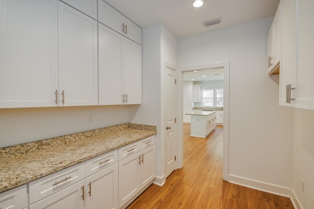 bar with light stone countertops, light hardwood / wood-style flooring, and white cabinets