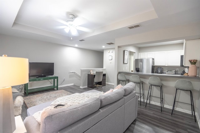 living room featuring dark hardwood / wood-style flooring, a tray ceiling, and ceiling fan