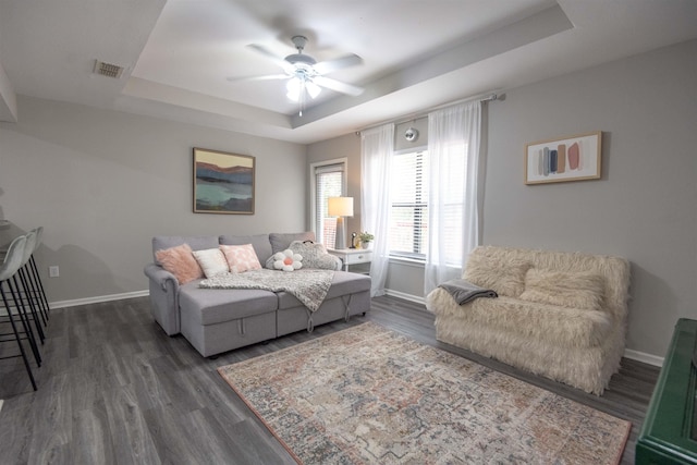 living room with a raised ceiling, dark wood-type flooring, and ceiling fan