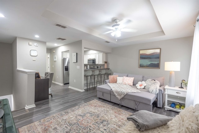 living room featuring dark wood-type flooring, ceiling fan, and a tray ceiling