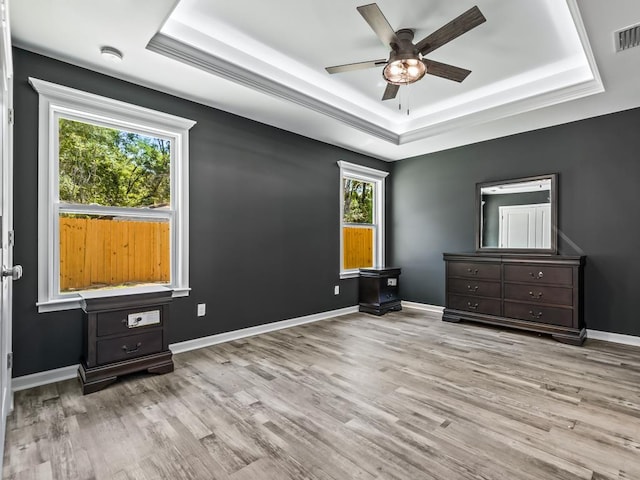 unfurnished bedroom featuring ceiling fan, light wood-type flooring, and a tray ceiling