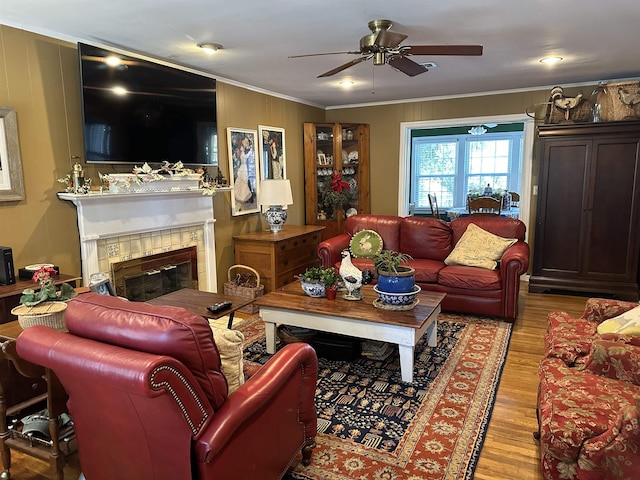 living room with light wood-type flooring, ceiling fan, crown molding, and a tiled fireplace