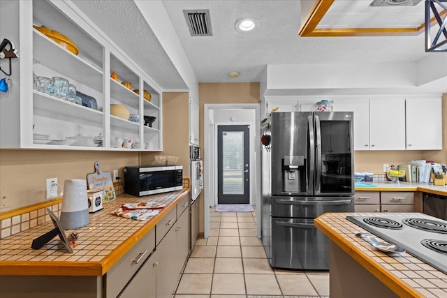 kitchen with tile countertops, white cabinets, stainless steel appliances, and a textured ceiling