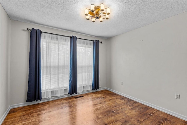 unfurnished room featuring an inviting chandelier, a textured ceiling, and hardwood / wood-style flooring