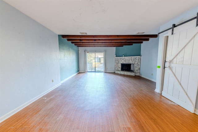 unfurnished living room featuring beam ceiling, a barn door, light wood-type flooring, and a fireplace