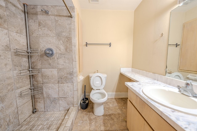 bathroom with toilet, a tile shower, and vanity