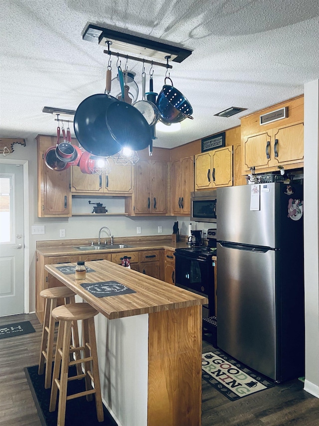 kitchen with a textured ceiling, sink, stainless steel appliances, and dark wood-type flooring