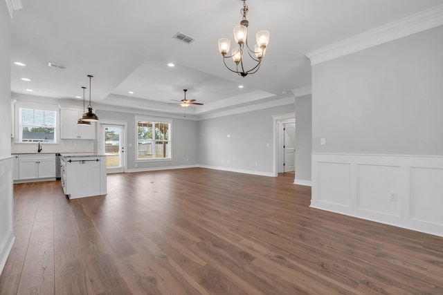 unfurnished living room featuring ceiling fan with notable chandelier, a raised ceiling, dark wood-type flooring, crown molding, and sink