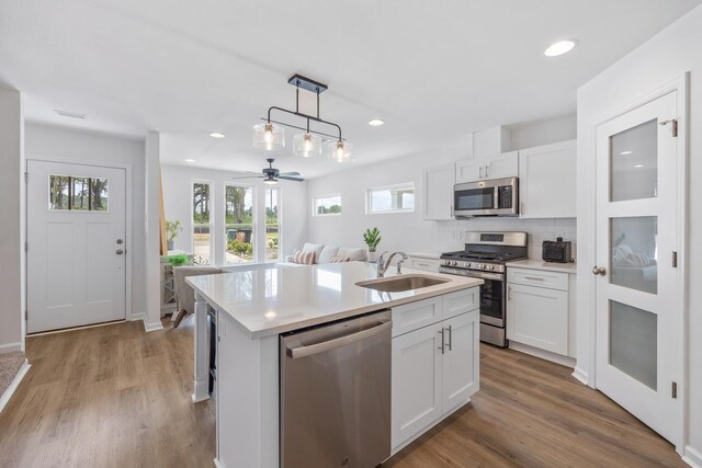 kitchen featuring white cabinetry, ceiling fan, hanging light fixtures, stainless steel appliances, and an island with sink