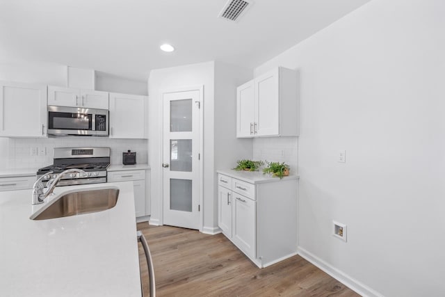 kitchen featuring appliances with stainless steel finishes, light wood-type flooring, backsplash, sink, and white cabinets