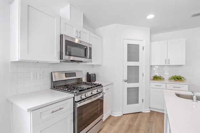 kitchen with white cabinets, light wood-type flooring, and appliances with stainless steel finishes