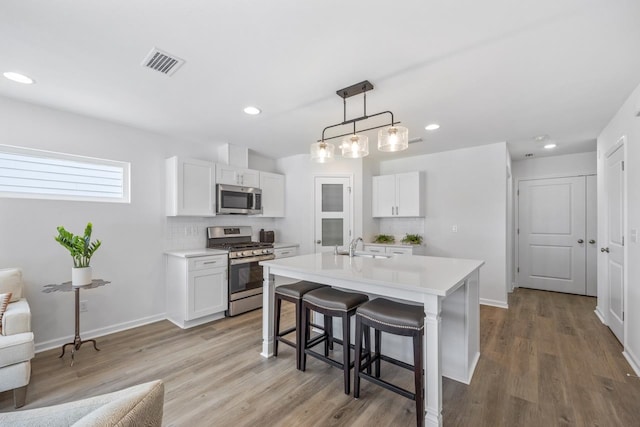 kitchen with white cabinets, appliances with stainless steel finishes, decorative backsplash, and decorative light fixtures