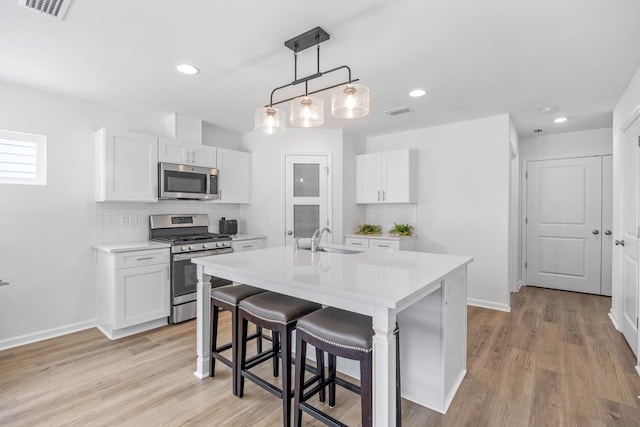 kitchen featuring an island with sink, stainless steel appliances, white cabinetry, and sink