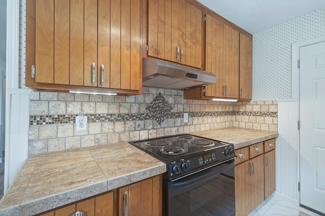 2903 Whirlaway Trl, Tallahassee, FL 32309 - kitchen featuring black electric range oven, under cabinet range hood, brown cabinets, decorative backsplash, and wallpapered walls