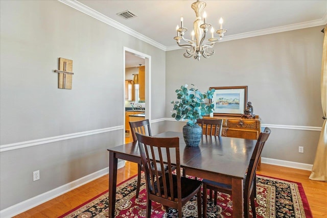 dining area with sink, hardwood / wood-style flooring, crown molding, and an inviting chandelier