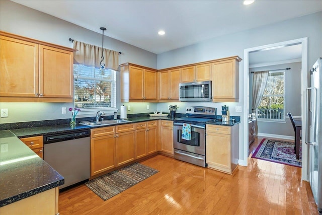 kitchen with light hardwood / wood-style floors, dark stone counters, sink, decorative light fixtures, and stainless steel appliances