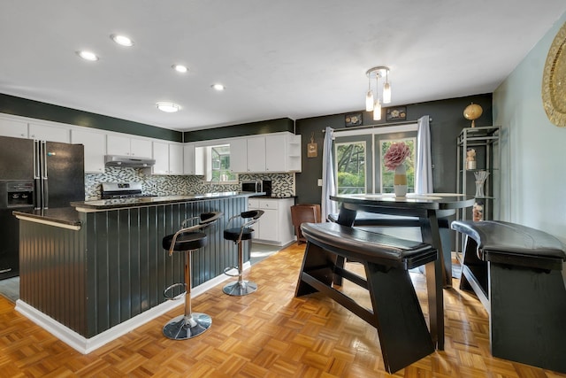 kitchen featuring white cabinets, stainless steel stove, black refrigerator with ice dispenser, and decorative light fixtures