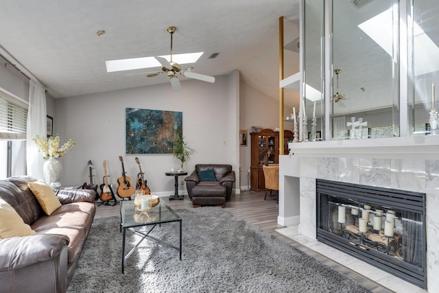 living area featuring visible vents, lofted ceiling with skylight, baseboards, and a high end fireplace