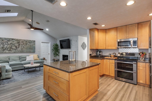 kitchen featuring light wood-style floors, appliances with stainless steel finishes, open floor plan, and a high end fireplace