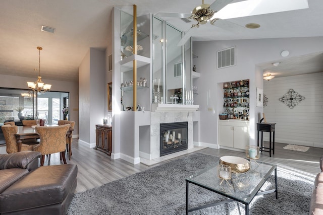 living area featuring visible vents, wood finished floors, a premium fireplace, and ceiling fan with notable chandelier