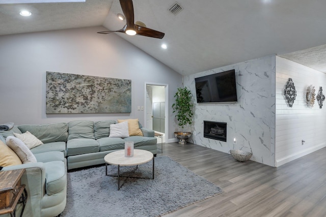 living area featuring a ceiling fan, wood finished floors, visible vents, baseboards, and a high end fireplace