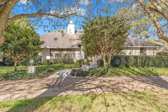 view of front of house featuring roof with shingles, a chimney, and a front lawn