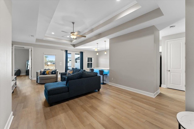 living room with a tray ceiling, light hardwood / wood-style floors, french doors, and ceiling fan