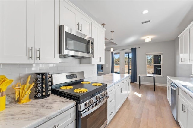 kitchen with pendant lighting, white cabinetry, stainless steel appliances, tasteful backsplash, and light wood-type flooring