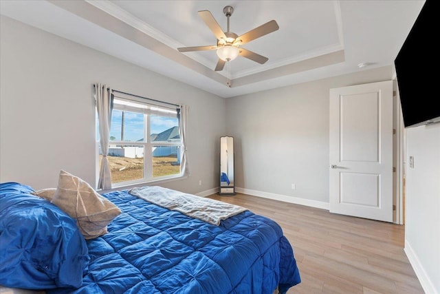 bedroom with ceiling fan, ornamental molding, a tray ceiling, and light hardwood / wood-style flooring