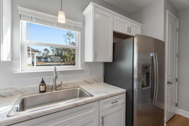 kitchen with sink, stainless steel fridge, white cabinets, decorative backsplash, and hanging light fixtures