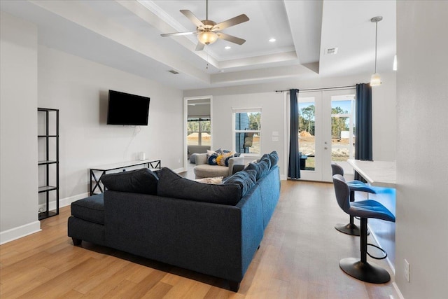 living room with french doors, a tray ceiling, light hardwood / wood-style floors, and a wealth of natural light