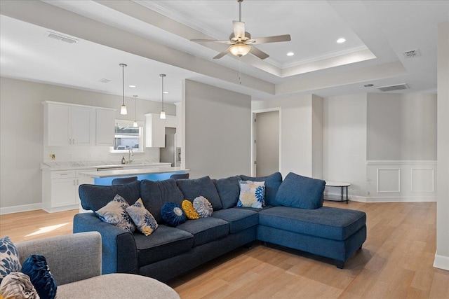 living room with crown molding, ceiling fan, a raised ceiling, and light hardwood / wood-style flooring