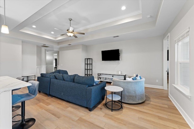 living room featuring crown molding, ceiling fan, a tray ceiling, and light hardwood / wood-style flooring