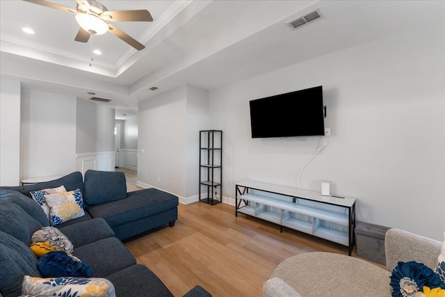 living room with hardwood / wood-style flooring, ceiling fan, ornamental molding, and a tray ceiling