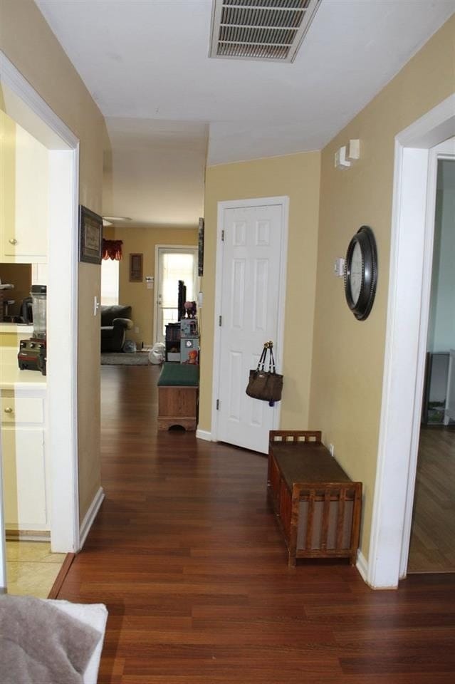 hallway featuring dark wood-style flooring, visible vents, and baseboards