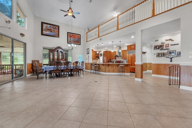 interior space with wood walls, a towering ceiling, and ceiling fan with notable chandelier