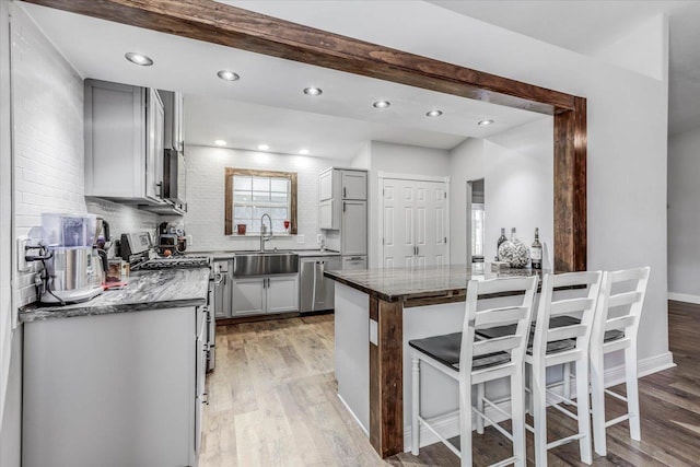 kitchen with gray cabinets, sink, kitchen peninsula, stainless steel gas range, and light hardwood / wood-style flooring