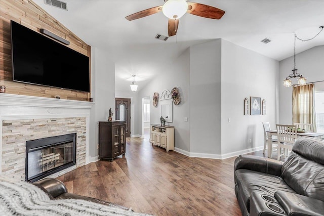 living room with ceiling fan with notable chandelier, wood-type flooring, a stone fireplace, and vaulted ceiling