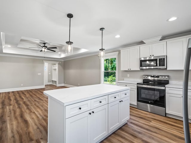 kitchen with ornamental molding, appliances with stainless steel finishes, pendant lighting, white cabinets, and a tray ceiling