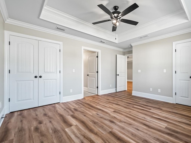 unfurnished bedroom featuring crown molding, hardwood / wood-style flooring, ceiling fan, and a raised ceiling