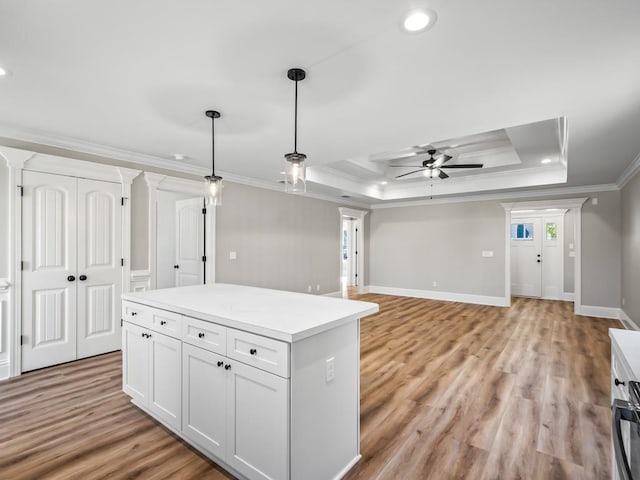 kitchen featuring white cabinets, ornamental molding, a raised ceiling, pendant lighting, and light hardwood / wood-style flooring