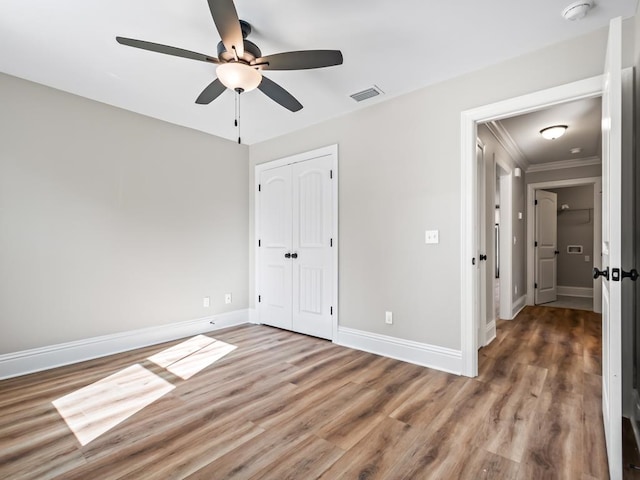 unfurnished bedroom with ceiling fan, a closet, crown molding, and wood-type flooring