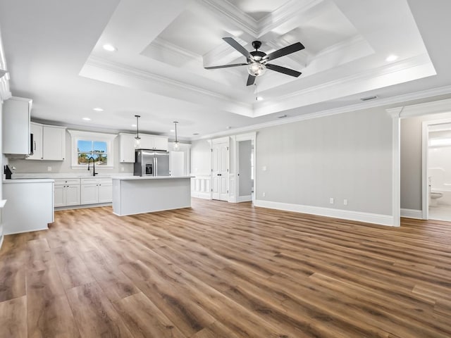 unfurnished living room featuring wood-type flooring, a tray ceiling, sink, and ornamental molding