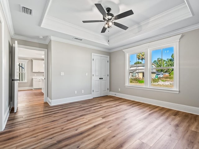 unfurnished bedroom featuring a closet, wood-type flooring, crown molding, a raised ceiling, and ceiling fan