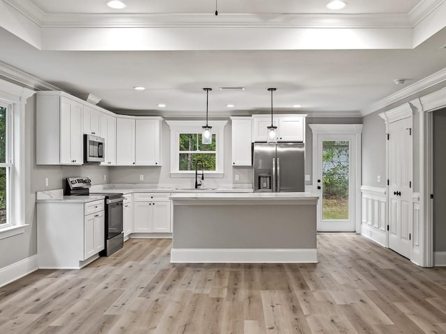 kitchen featuring hanging light fixtures, stainless steel appliances, light hardwood / wood-style floors, white cabinets, and ornamental molding