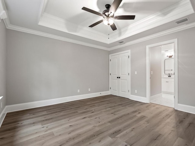 unfurnished bedroom featuring a tray ceiling, ensuite bath, ceiling fan, and ornamental molding