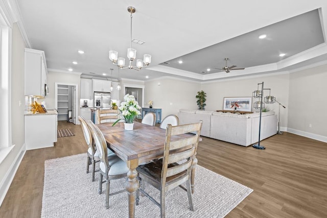 dining area featuring crown molding, a tray ceiling, ceiling fan with notable chandelier, and hardwood / wood-style floors