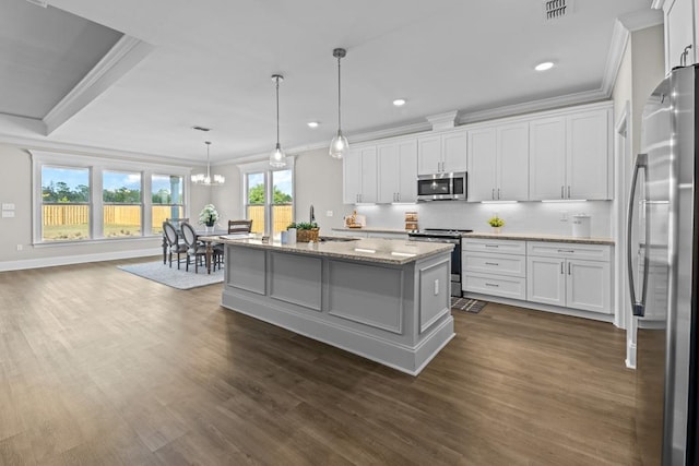 kitchen featuring appliances with stainless steel finishes, white cabinetry, hanging light fixtures, a kitchen island with sink, and light stone countertops