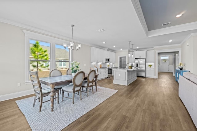 dining space featuring an inviting chandelier, crown molding, sink, and light hardwood / wood-style flooring