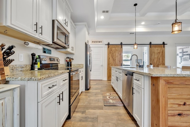 kitchen featuring a barn door, a sink, stainless steel appliances, white cabinetry, and visible vents